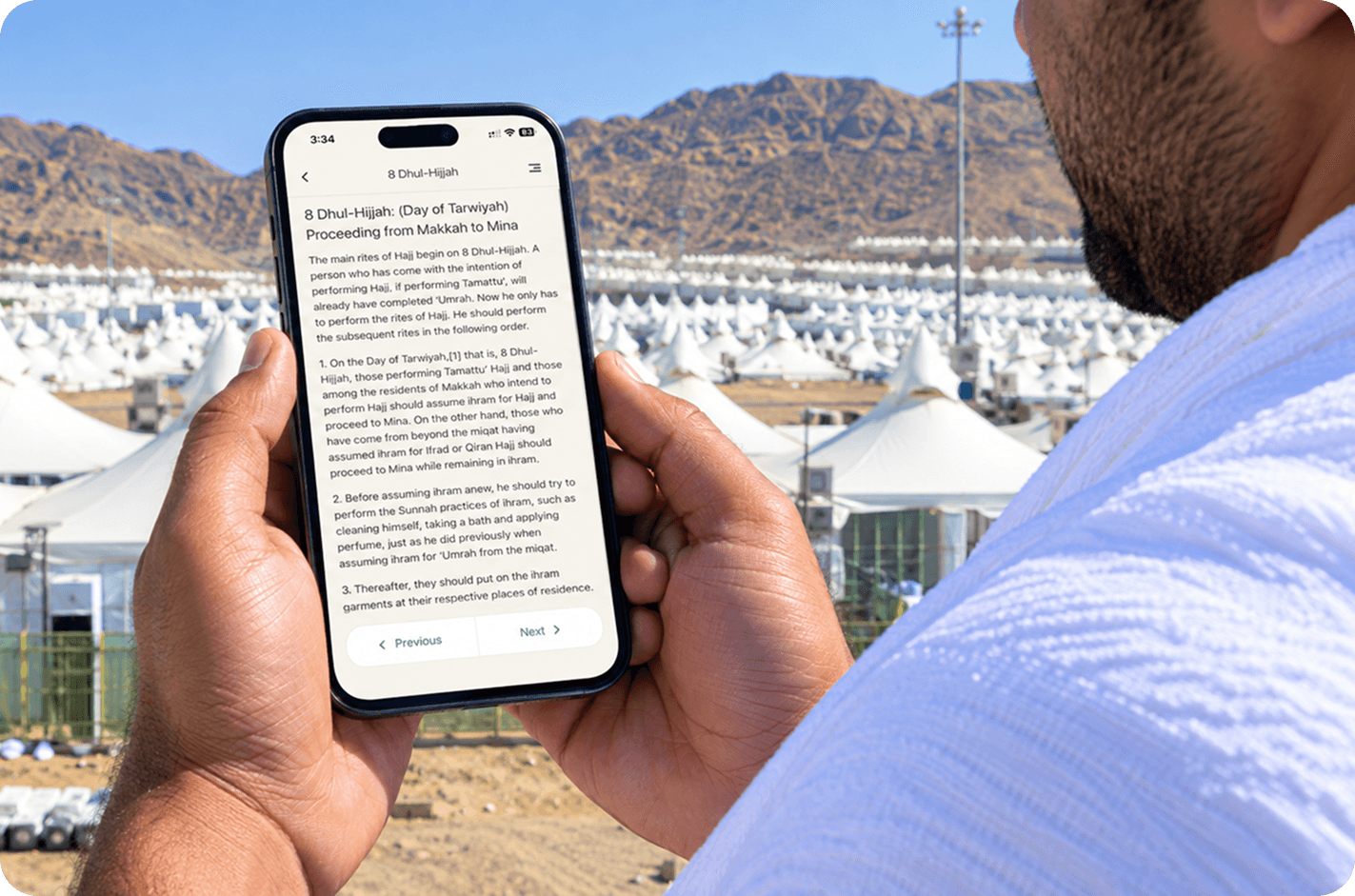 A pilgrim in ihram reading the app’s Hajj day guide, standing above the tents at Mina
